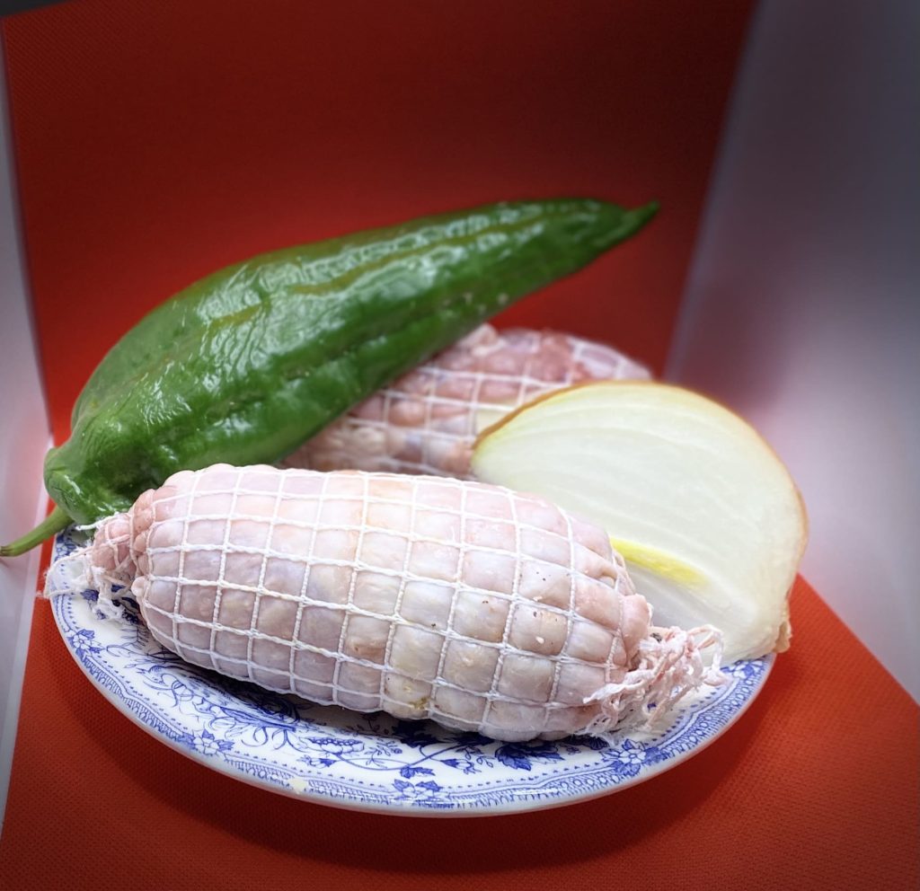 Muslos de pollo rellenos atado con cuerda acompañado con rodaja de cebolla y pimiento verde sobre plato de diseño con fondo rojo.